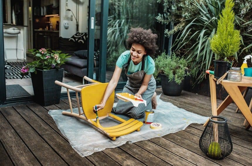 A Female painting vintage chair in yellow color with a paintbrush